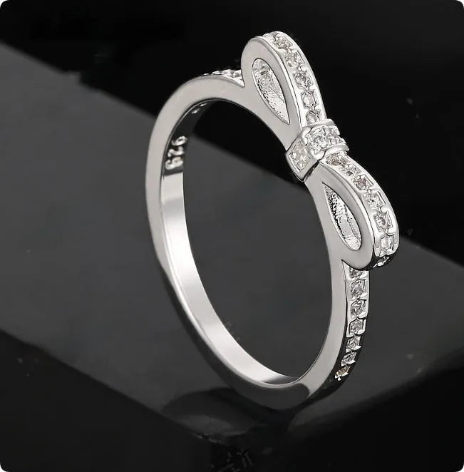 Silver-coloured bow-shaped ring with sparkling zircon crystals on a model's finger.