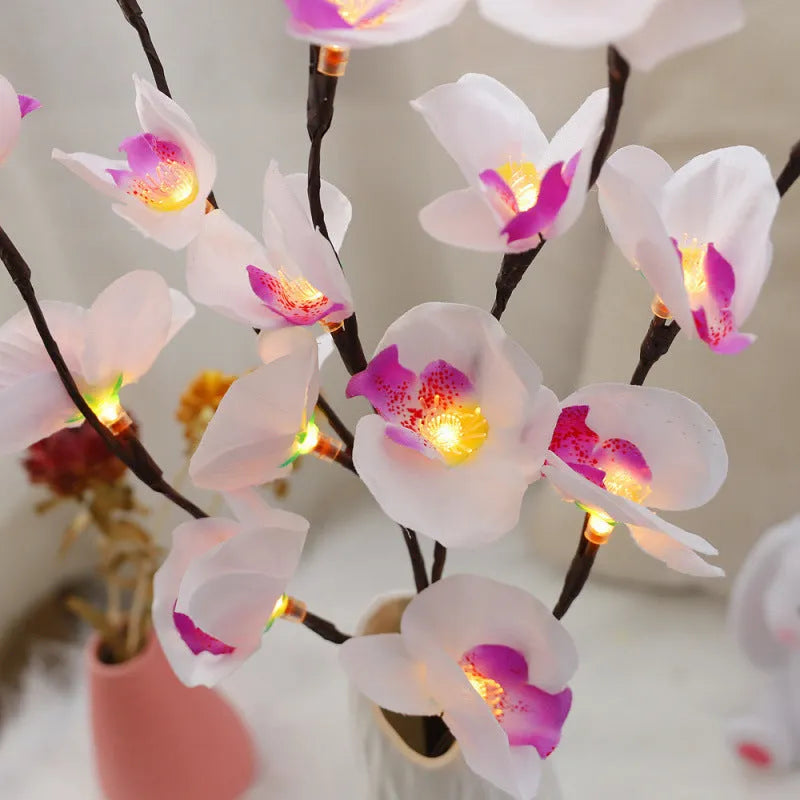 Pink LED phalaenopsis orchid branch light, 65cm tall, on a wooden surface emitting a warm glow.