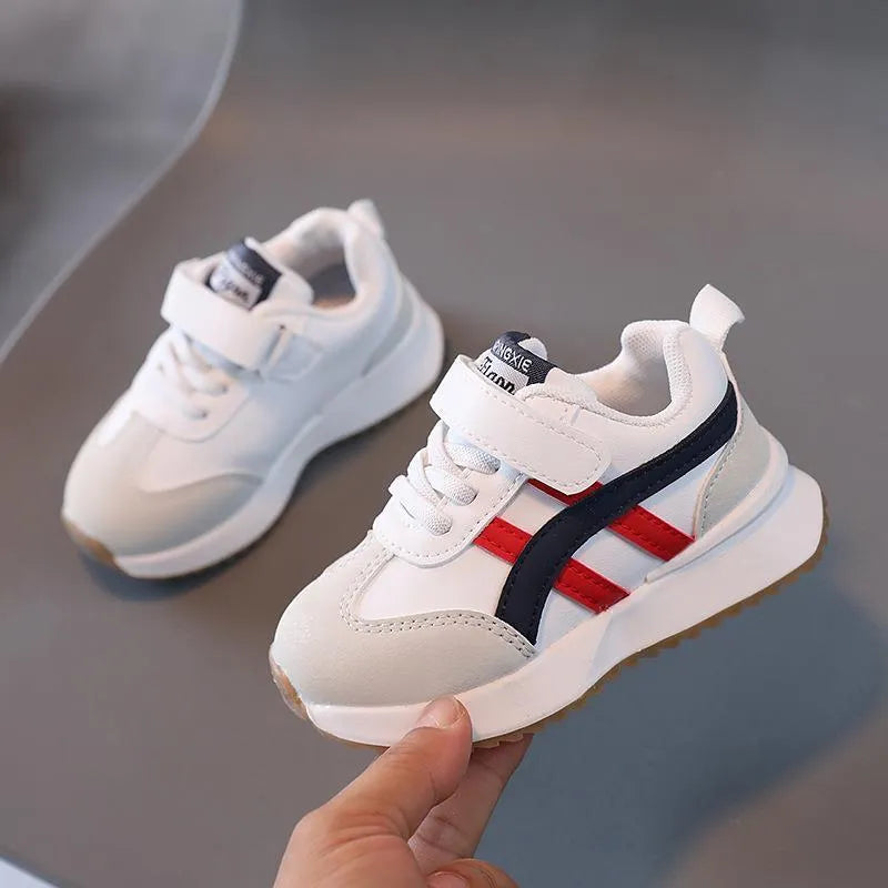 White children's sneakers with Velcro strap and textured rubber sole on a neutral background