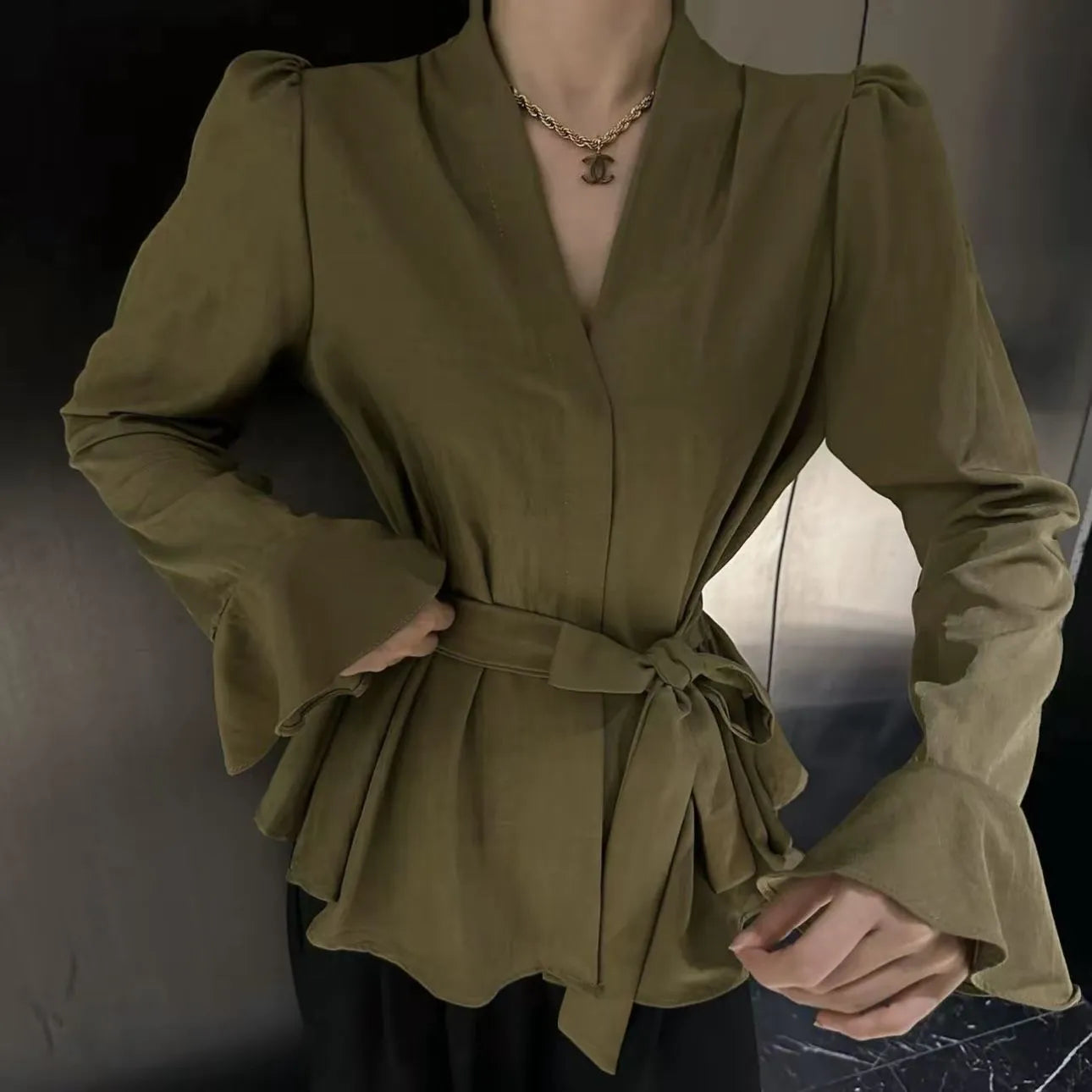 Woman wearing a black French-style shirt with an irregular collar, long bell sleeves, and a tie-front closure.