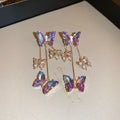 Long silver drop earrings with a blue-purple butterfly, crystal flowers, and a delicate tassel on a white background.