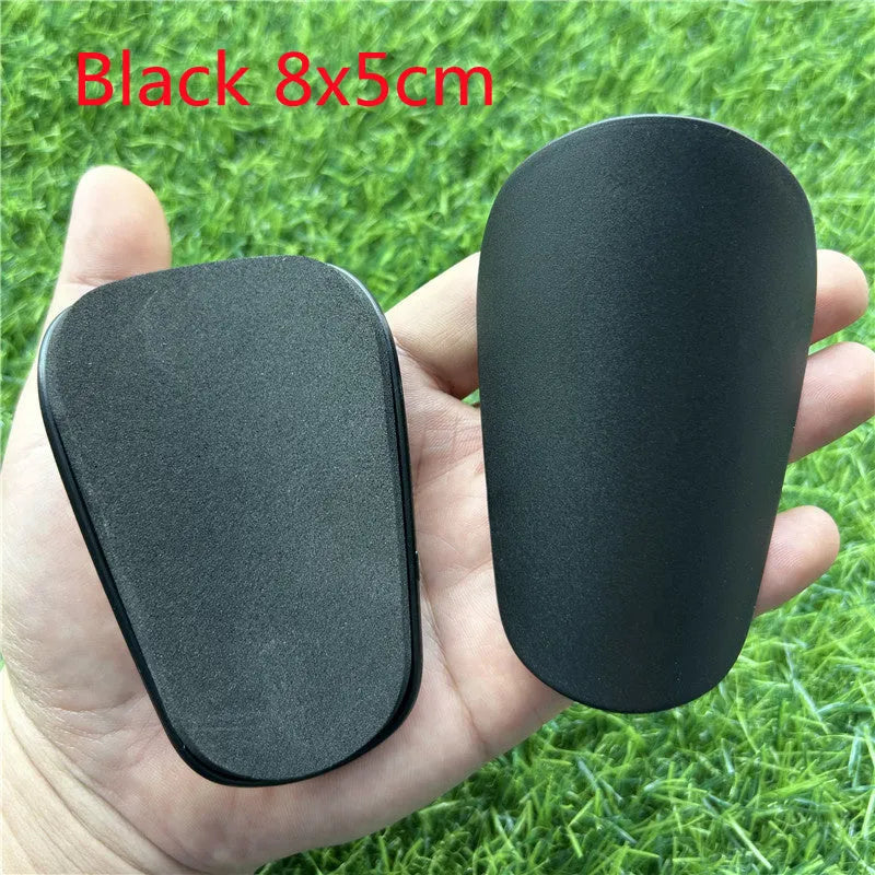 Extra small mini plastic football shin guards in black and white, shown at 8cm by 5cm size.