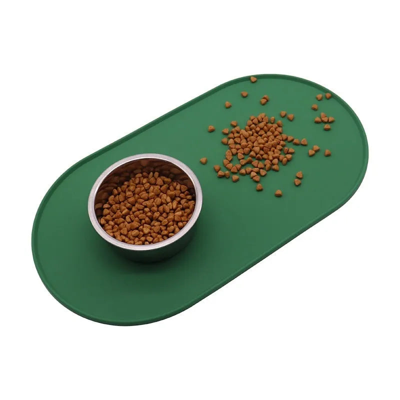 Green silicone cat feeding mat with raised edge containing a food bowl and scattered kibble on a kitchen floor.
