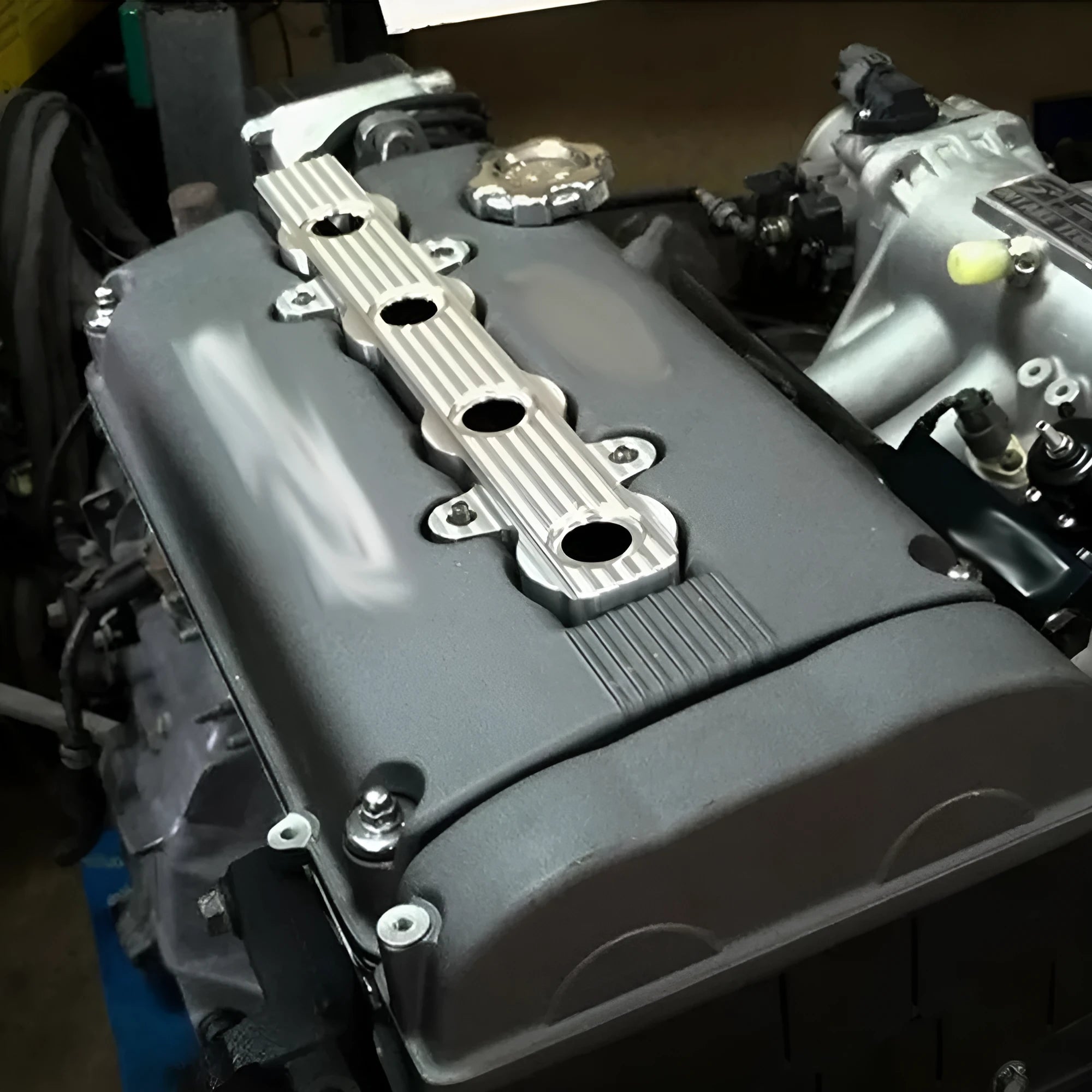 Aluminium engine harness housing bracket in blue, red, and silver, showing variants with and without mounting holes.