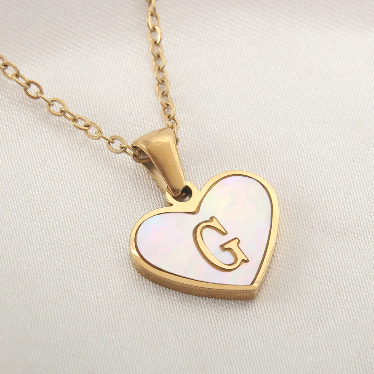 Gold-plated heart necklace with white shell pendant showing initial engraving on stainless steel chain