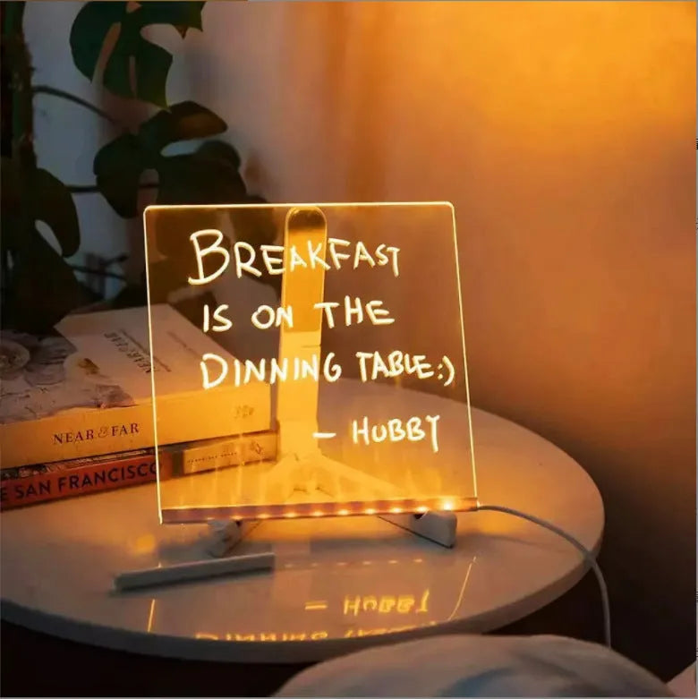 DIY acrylic message board LED night light on desk with colourful writing, USB cable, and pens