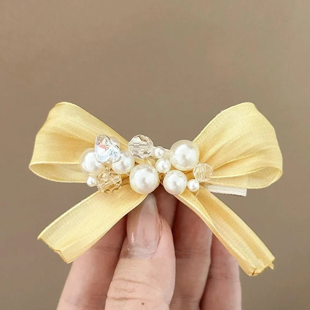Yellow bow hair barrette with rhinestone and pearl details on duckbill clip