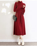 A woman wearing a rose red loose knitted turtleneck dress with a big hem midi skirt.