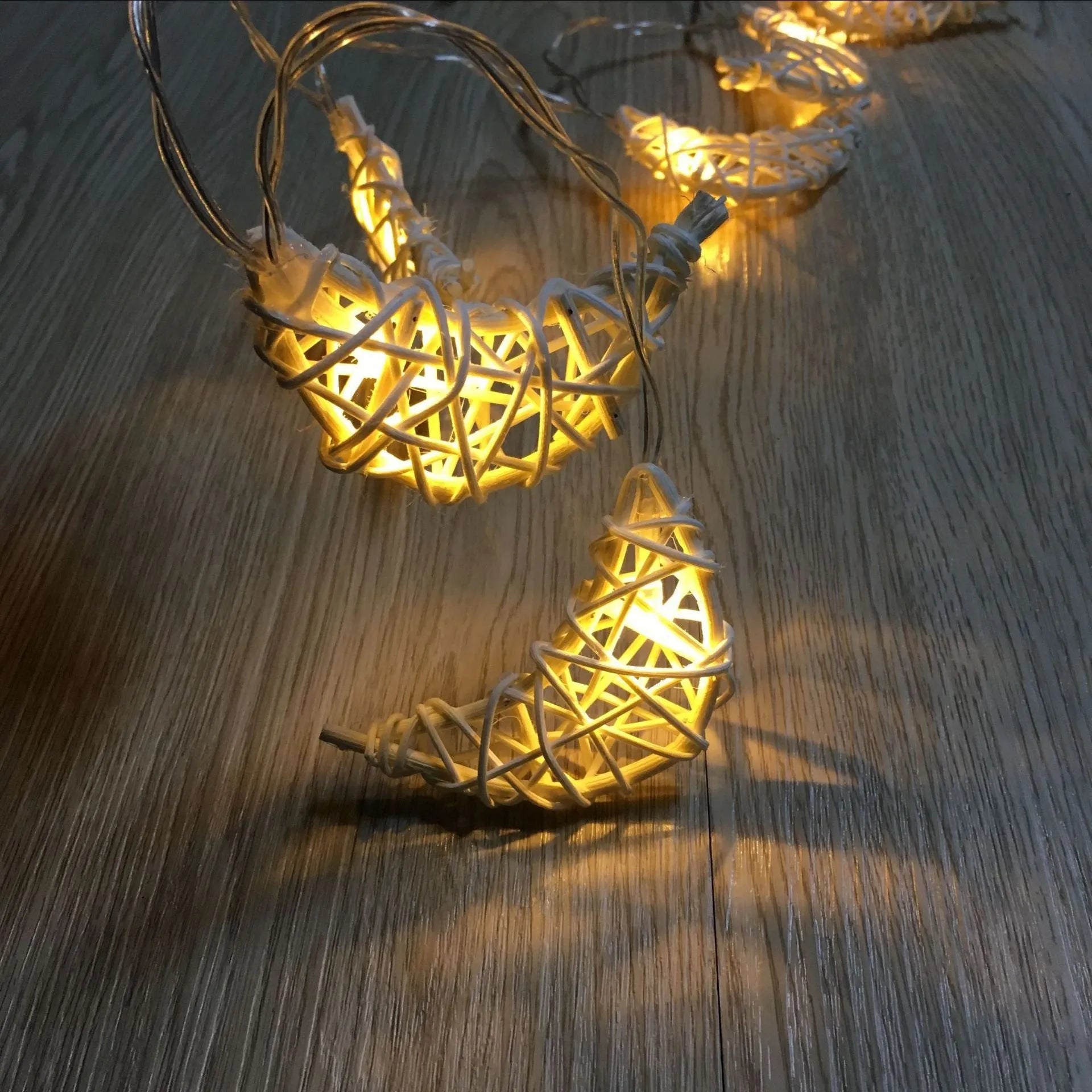 Handwoven rattan moon pendant fairy light chain with warm white glow on a dark background
