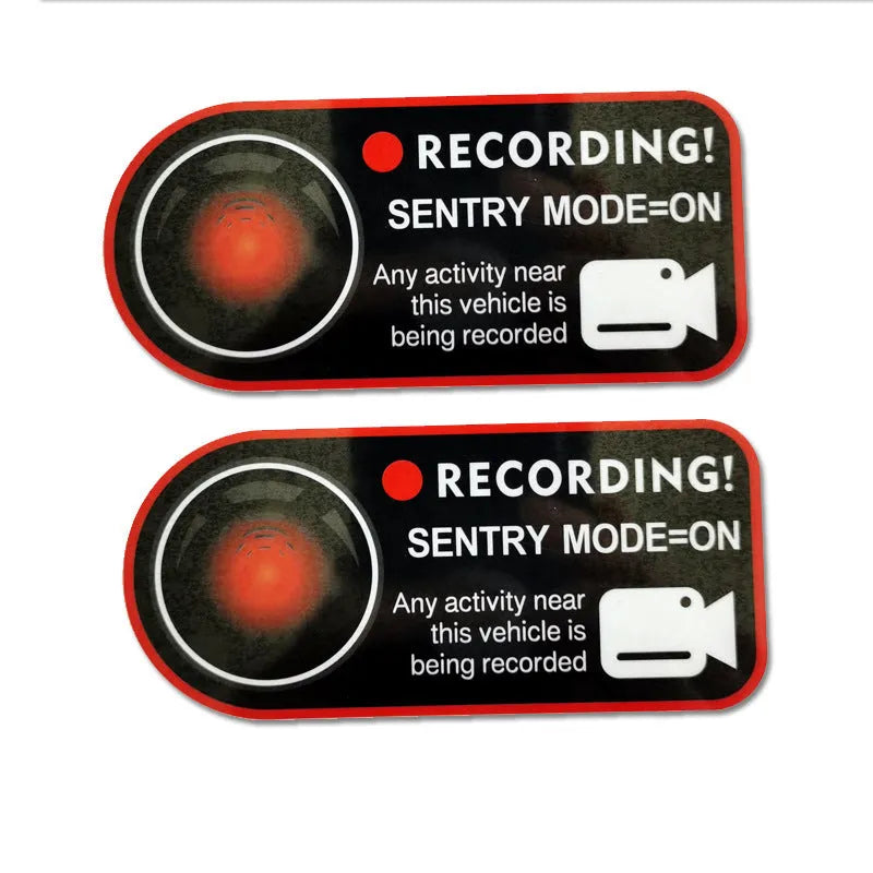A pair of white rectangular Tesla Sentry Mode warning stickers with black text, measuring 11cm by 5cm.