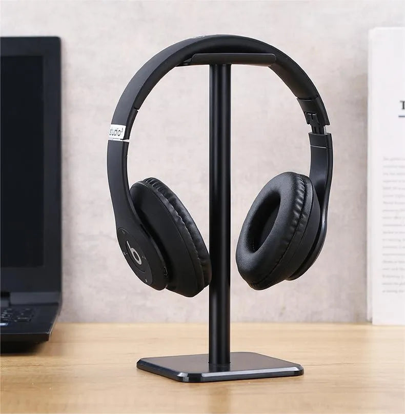 Detachable aluminum alloy headset hanger with TPU rubber cradle, shown in white, pink, and black, fixed to a table.