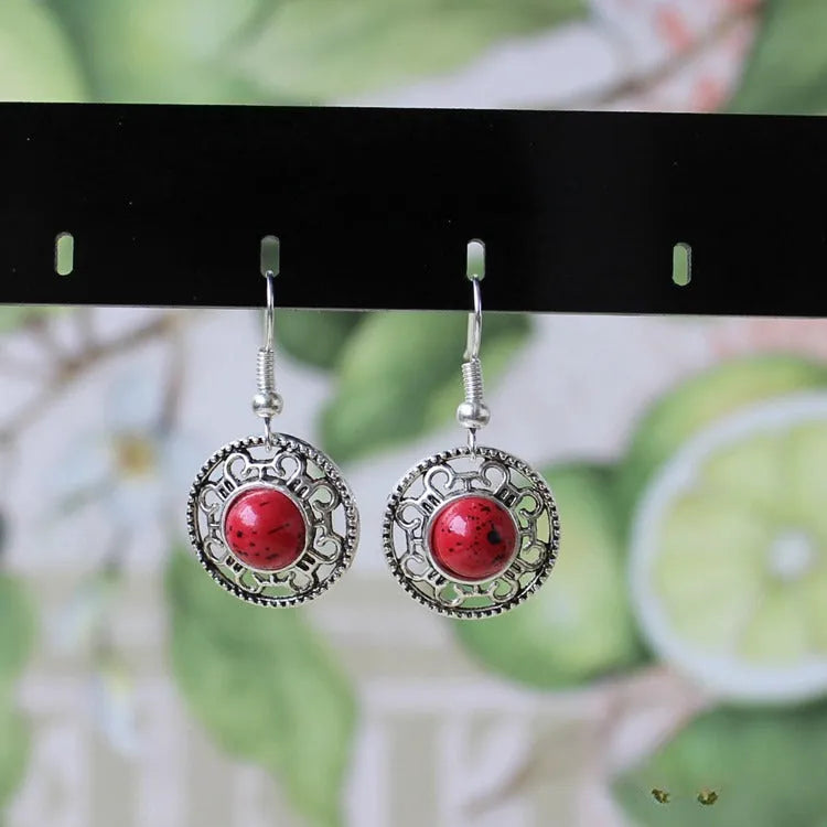 Handmade ethnic style earrings with a silver flower disk, turquoise stones, and red decorative patterns.