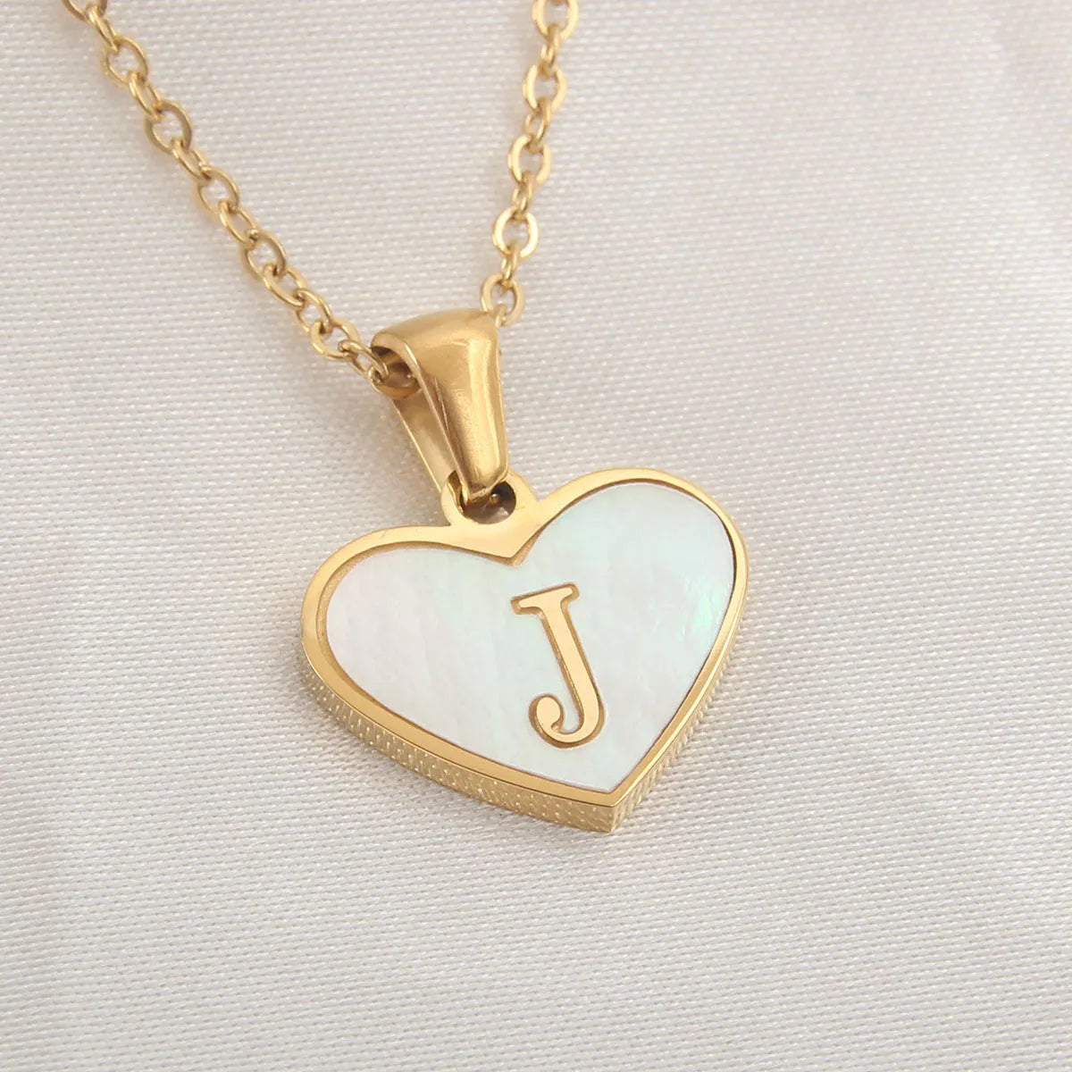 Gold-plated heart necklace with white shell pendant showing initial engraving on stainless steel chain
