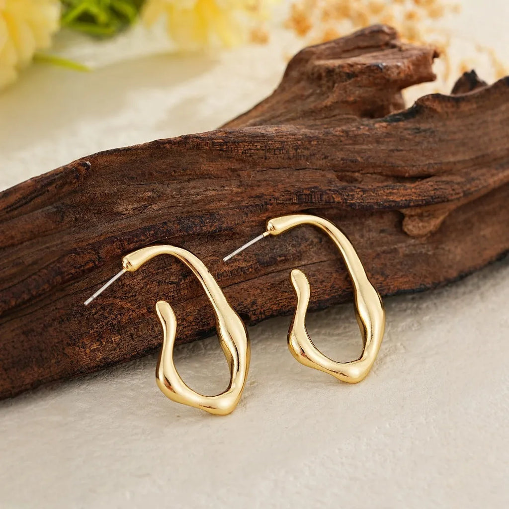 Gold irregular shaped minimalist drop earrings with abstract geometric design on neutral background