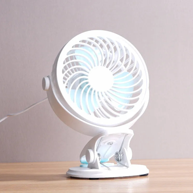 Small white USB desk fan with clip base and three blades on a wooden desk.