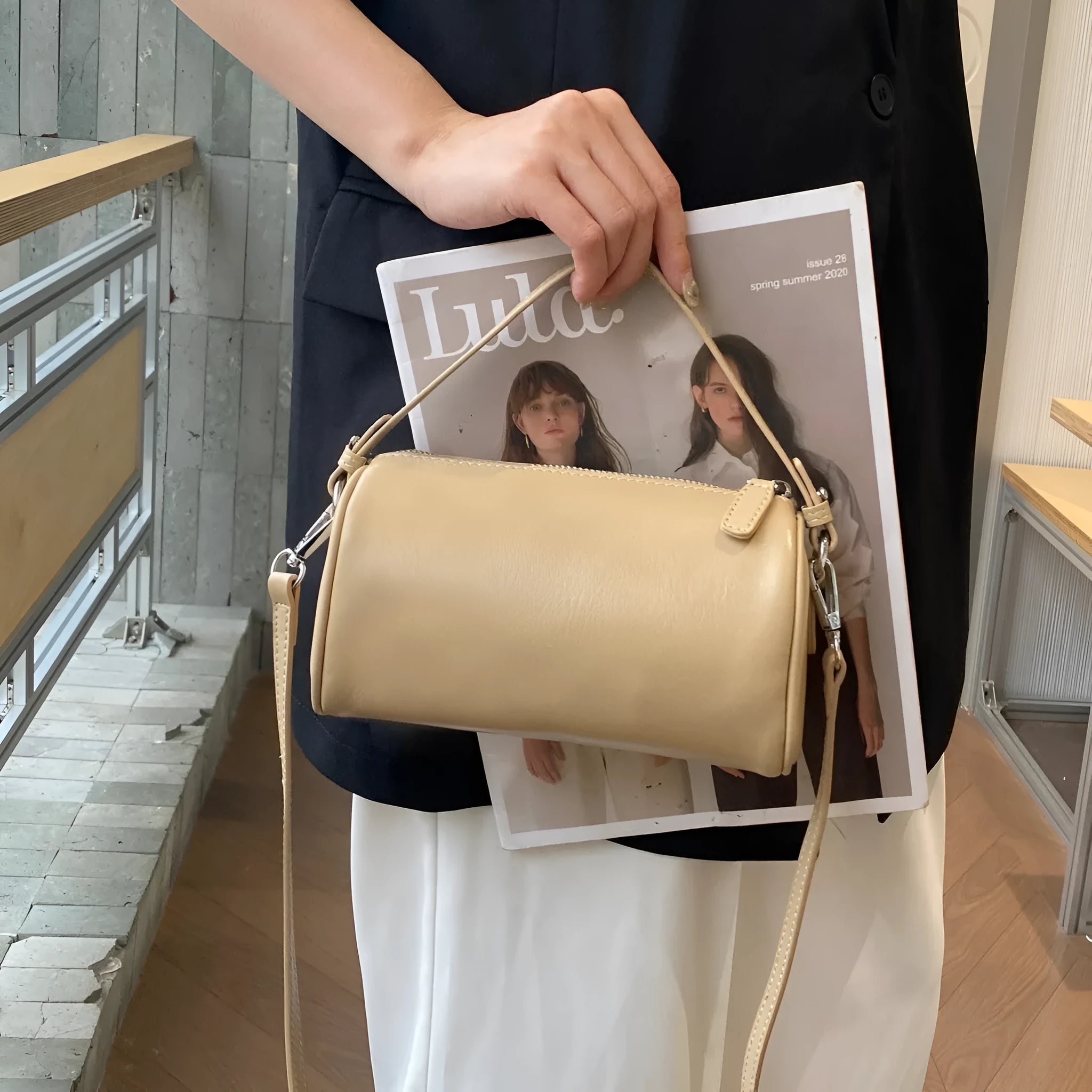 Genuine leather cylindrical crossbody phone bag in black, shown with single shoulder strap and visible sewing thread detail.