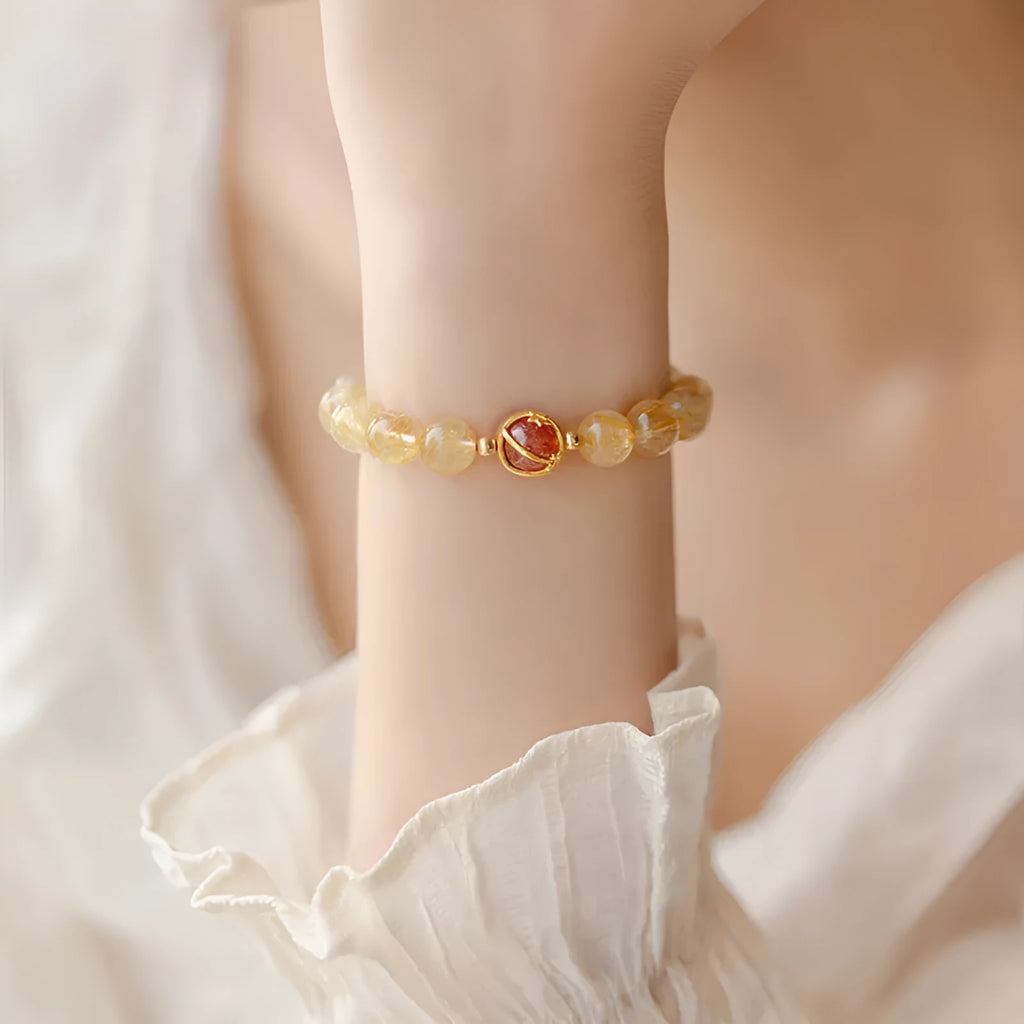 Citrine gold rutilated quartz crystal bracelet with diamond-cut beads on a wrist.