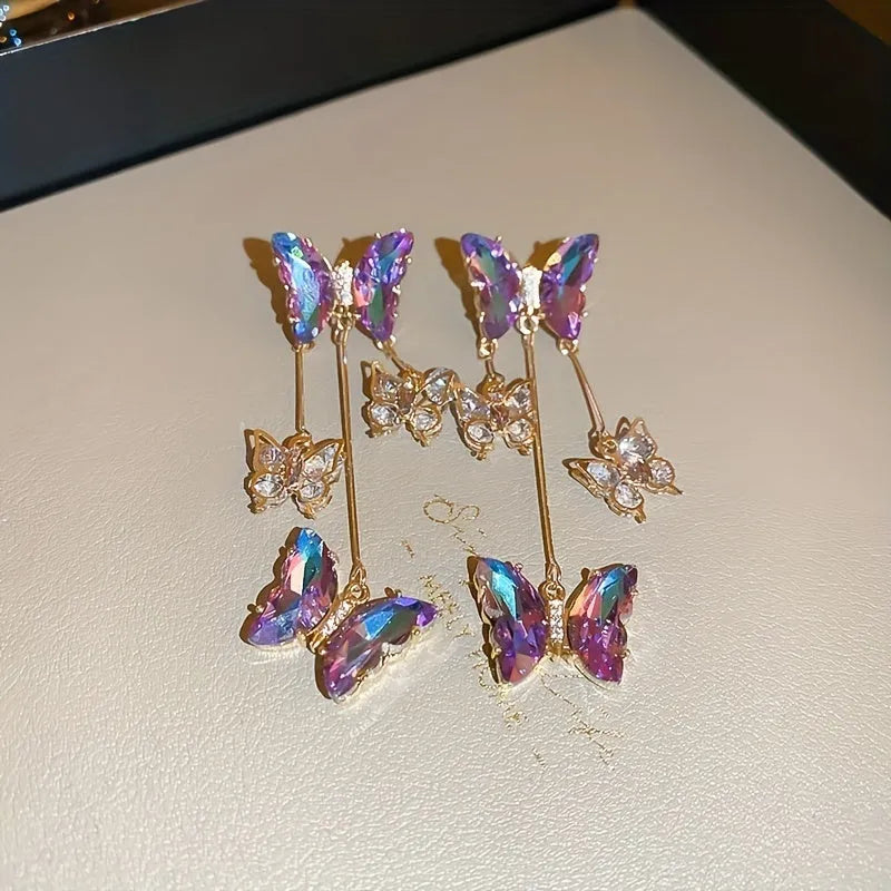 Long silver drop earrings with a blue-purple butterfly, crystal flowers, and a delicate tassel on a white background.