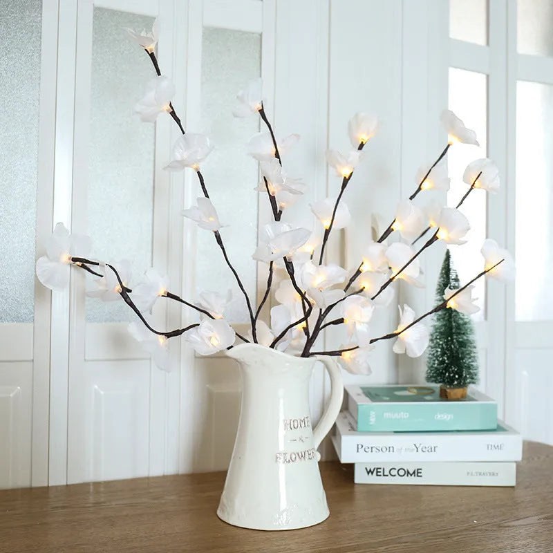 Pink LED phalaenopsis orchid branch light, 65cm tall, on a wooden surface emitting a warm glow.