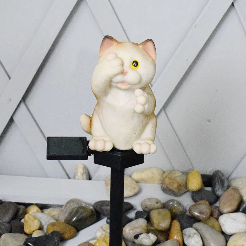 Brown resin cat-shaped solar garden light illuminating in a evening garden setting.