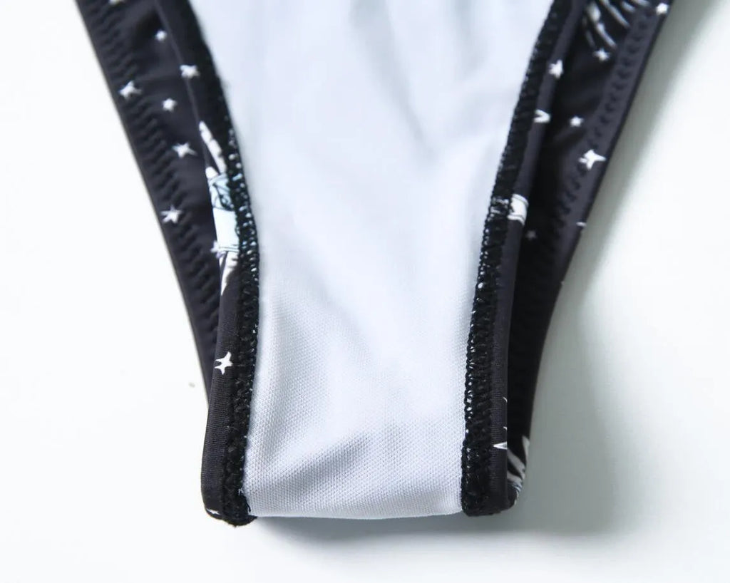 Black one-piece swimsuit with a printed bikini pattern, showing a split tube top and backless design.