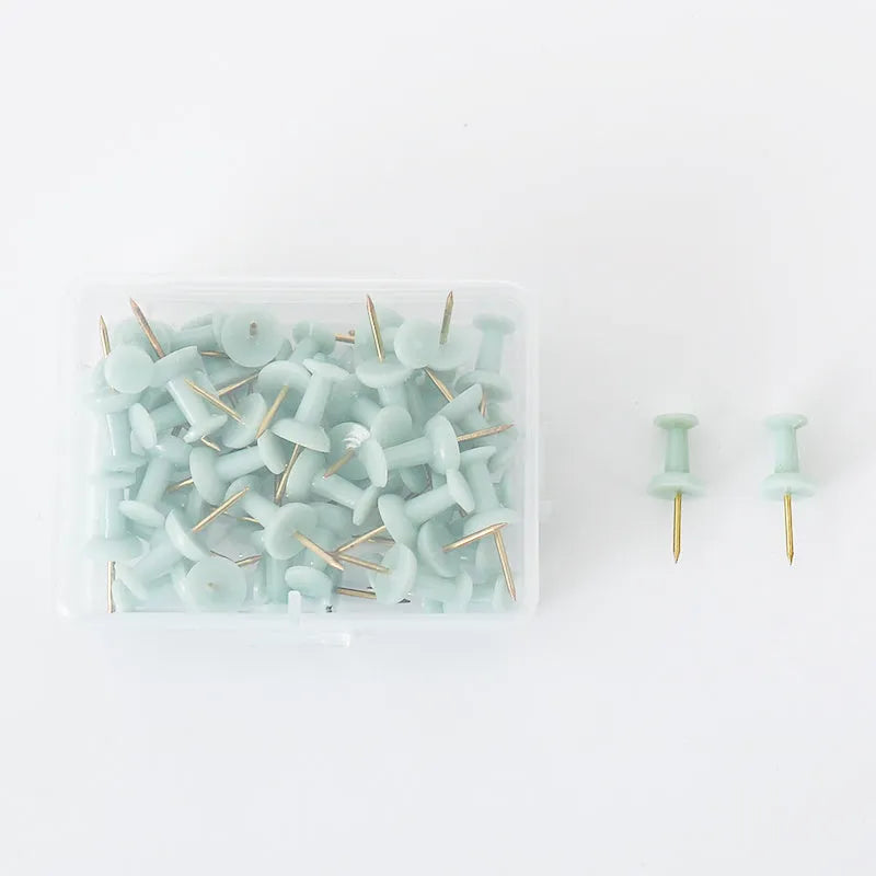Morandi colour push pins in green, grey, and pink with three different head designs on cork board
