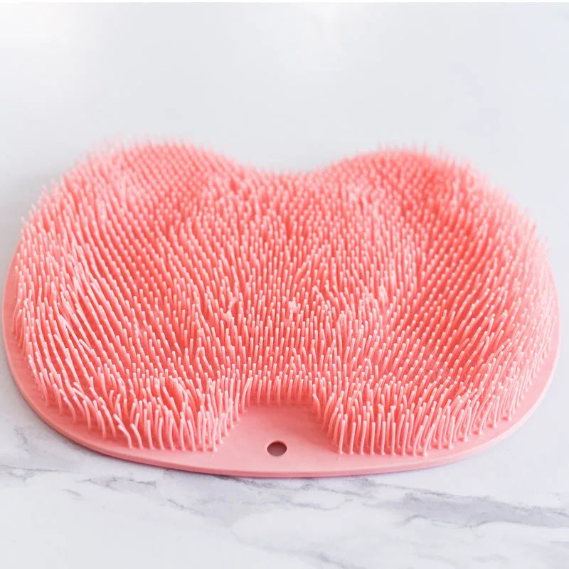 Orange non-slip bath brush with silicone bristles and suction cups on a bathroom floor.