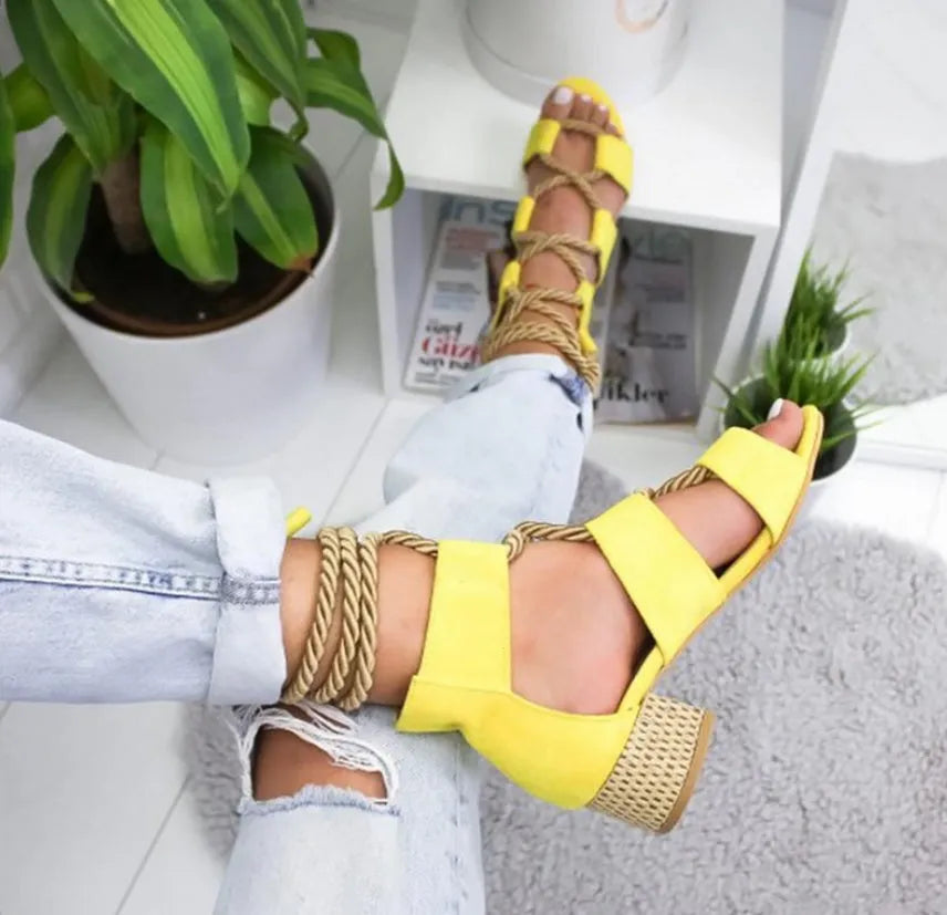 Women's beige suede sandals with thick heel and ankle strap on a foot.