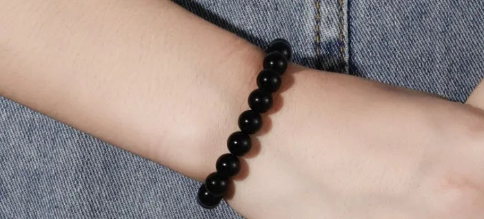 Close-up of a women's black agate bracelet with 8mm geometric beads on a black elastic cord.