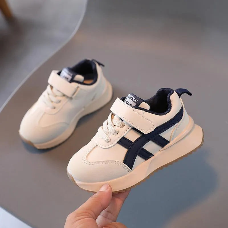 White children's sneakers with Velcro strap and textured rubber sole on a neutral background