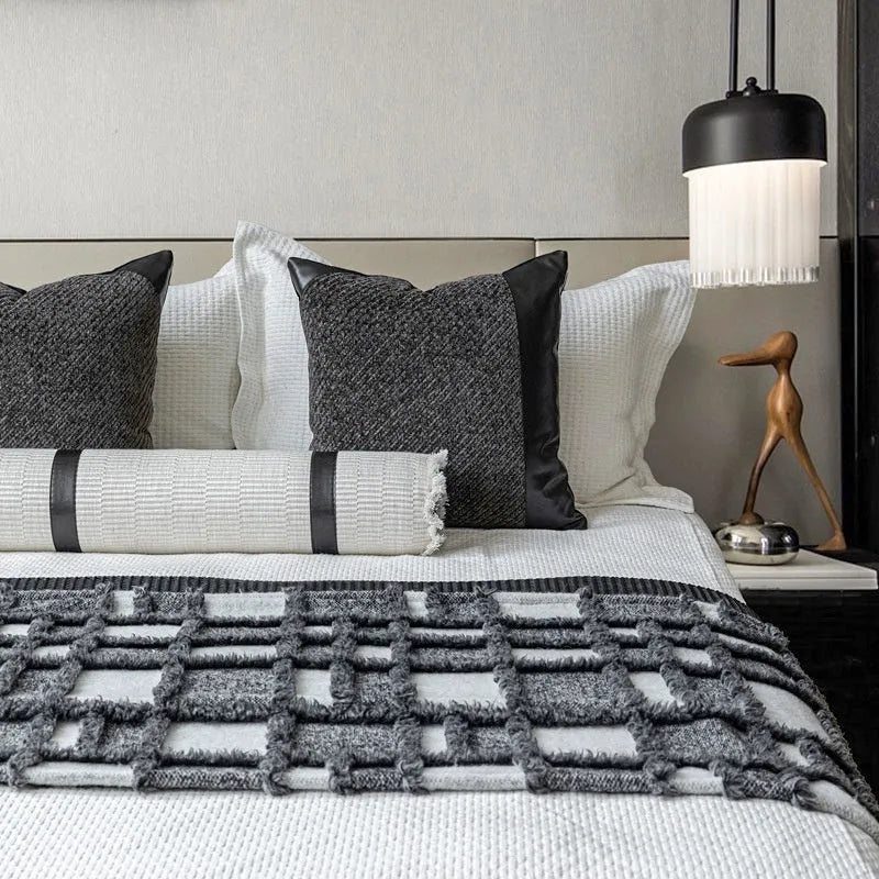 Modern gray and white plaid bed runner blanket with matching pillowcase and round leather-look pillow on a bed.