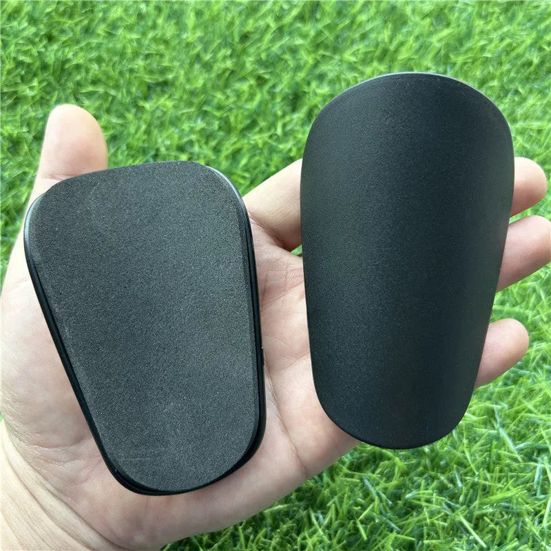 Extra small mini plastic football shin guards in black and white, shown at 8cm by 5cm size.