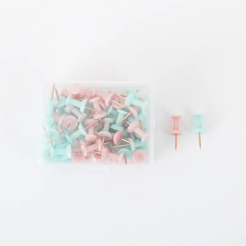 Morandi colour push pins in green, grey, and pink with three different head designs on cork board