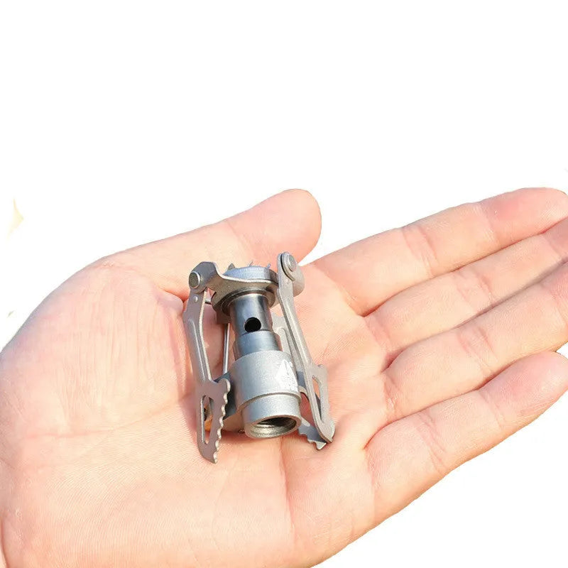 Compact portable camping stove with one-piece steel body and folded legs, shown with a propane canister.
