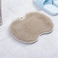 Orange non-slip bath brush with silicone bristles and suction cups on a bathroom floor.