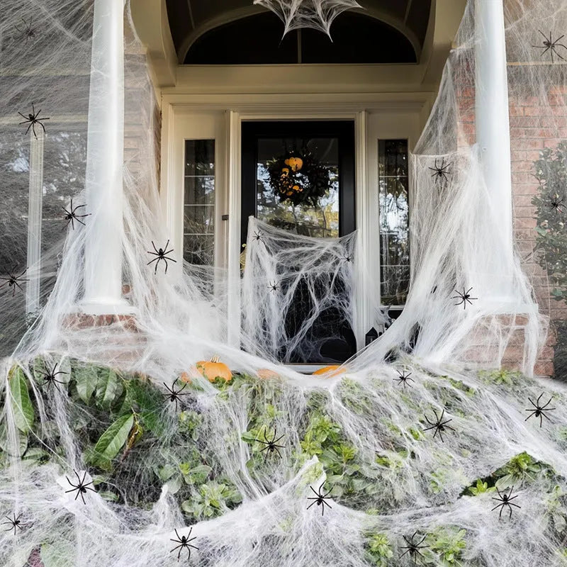 White cotton Halloween spider web decoration draped on a surface with scattered plastic spiders.