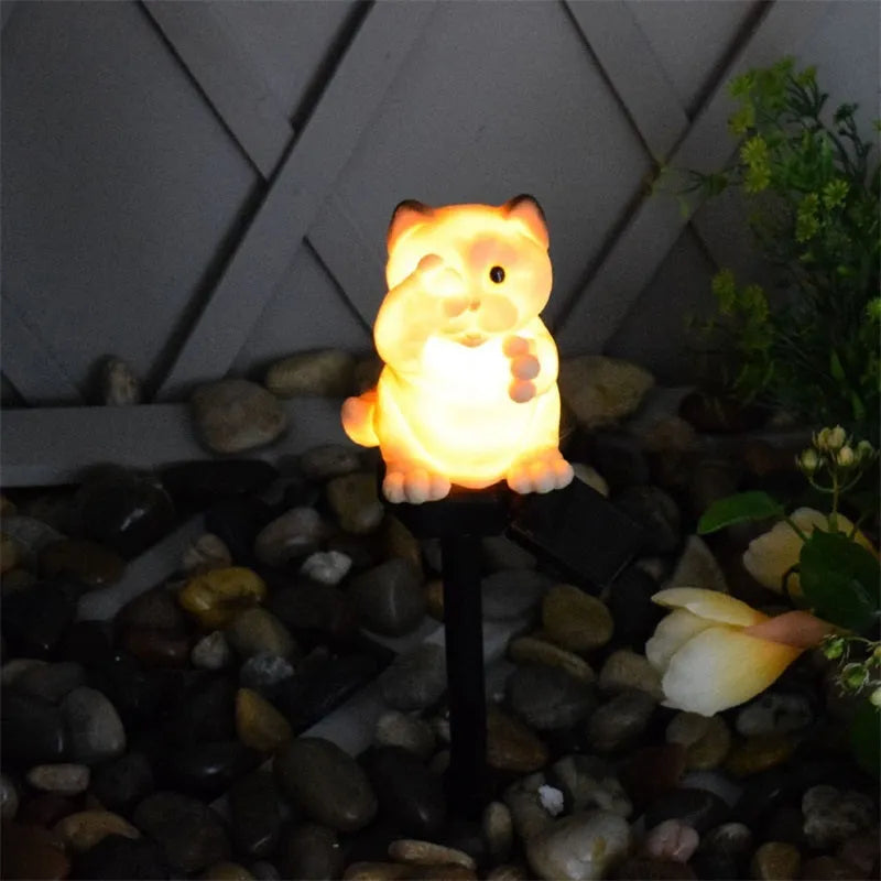 Brown resin cat-shaped solar garden light illuminating in a evening garden setting.