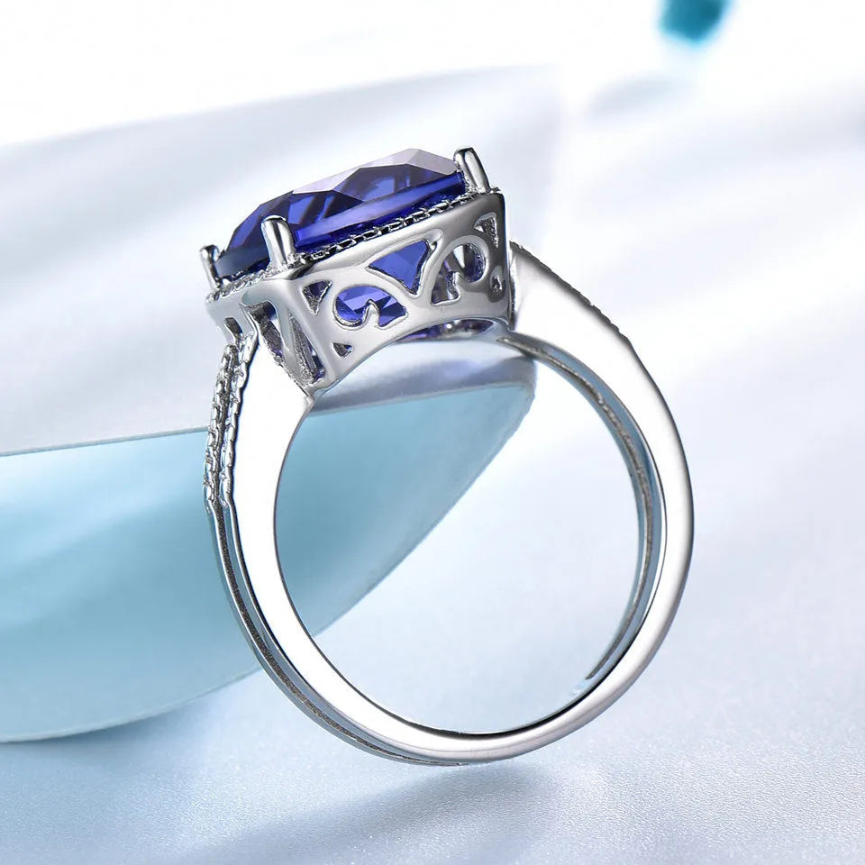 A sterling silver ring for women with a bright blue tanzanite stone, shown on a hand.
