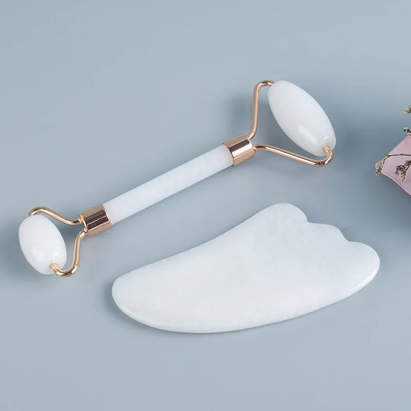 Natural white jade facial roller and gua sha scraper board set on a plain background.