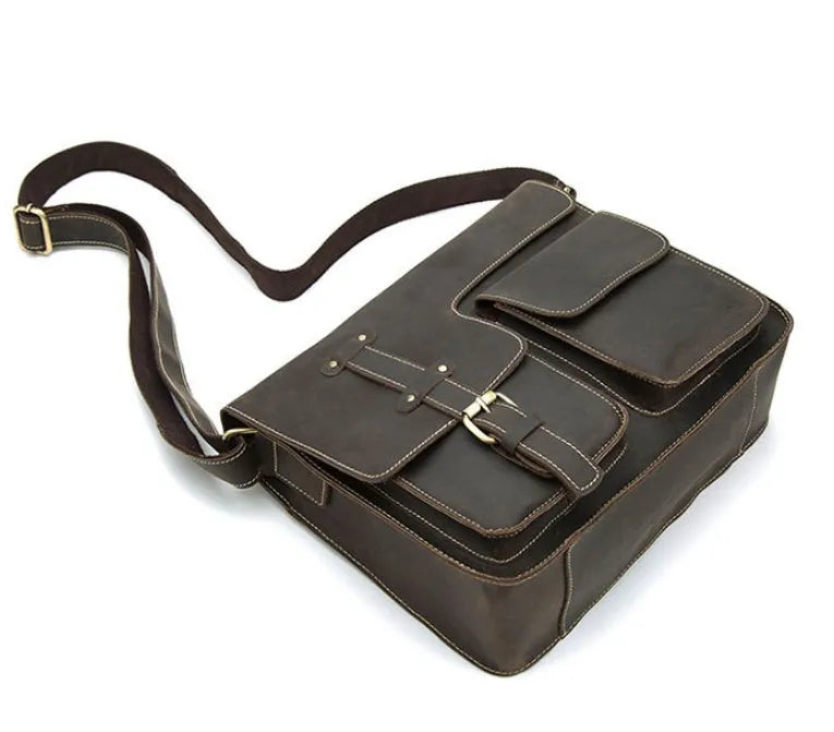 Brown full-grain leather vintage messenger bag with brass buckle, shown open to reveal padded laptop sleeve and internal pockets.