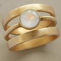 A gold-plated geometric ring with a hollow micro-inlaid white chalcedony stone on a titanium steel band.