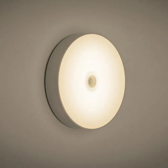 Small white circular motion sensing LED night light with USB charging cable and adhesive tape.