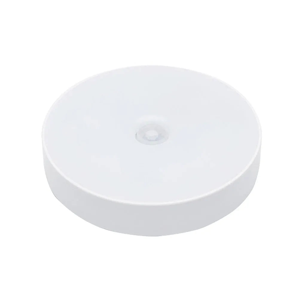 Small white circular motion sensing LED night light with USB charging cable and adhesive tape.