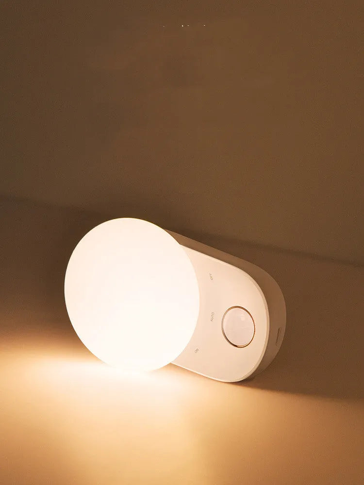 White Baseus rechargeable night light with motion sensor on a wooden bedside table.