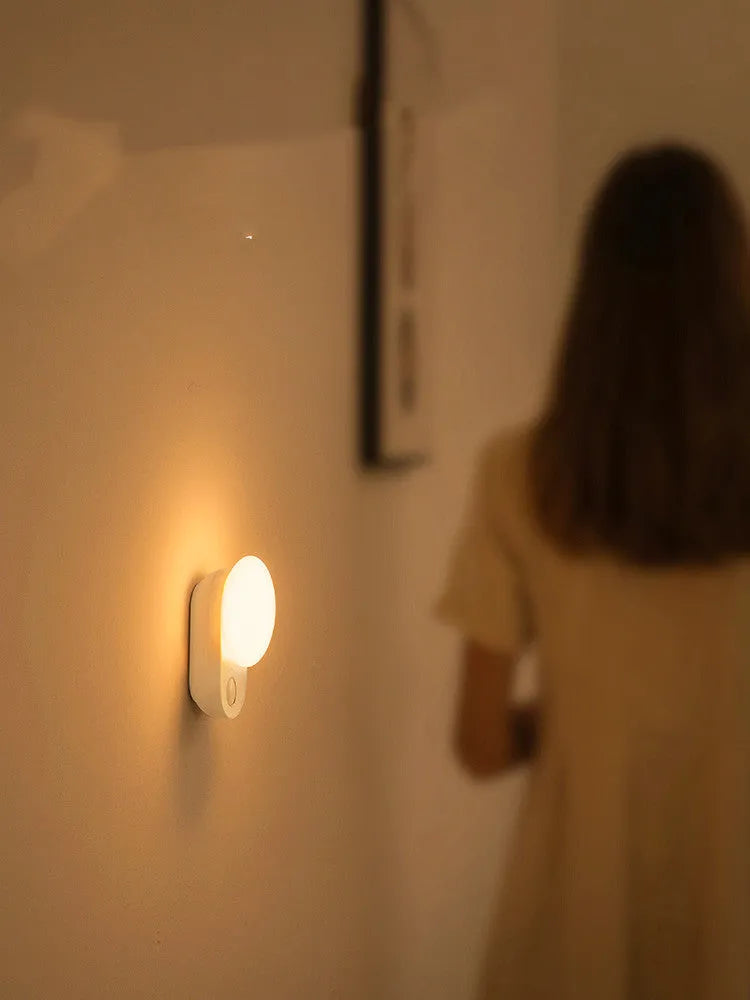 White Baseus rechargeable night light with motion sensor on a wooden bedside table.