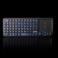 Black wireless mini keyboard with integrated optical mouse and USB receiver on a wooden desk