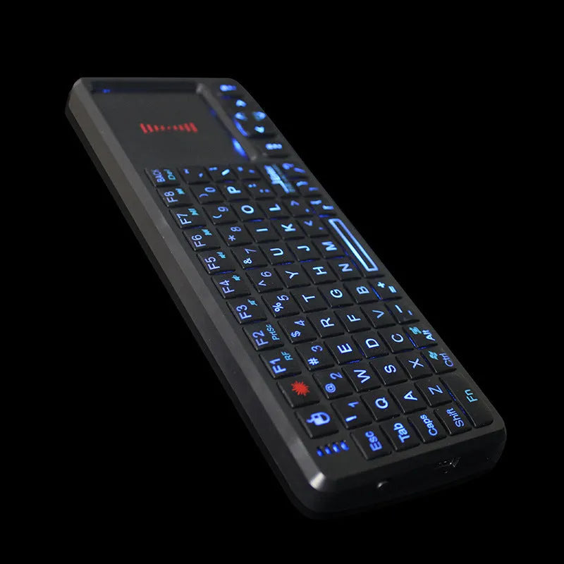 Black wireless mini keyboard with integrated optical mouse and USB receiver on a wooden desk