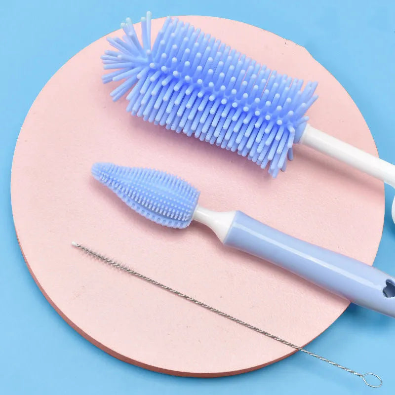 Three silicone baby bottle brushes in blue, pink, and yellow with straw scrubber on white background