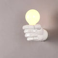Black resin fist wall lamp with integrated bulb holder, mounted on a brick wall, casting light downwards.