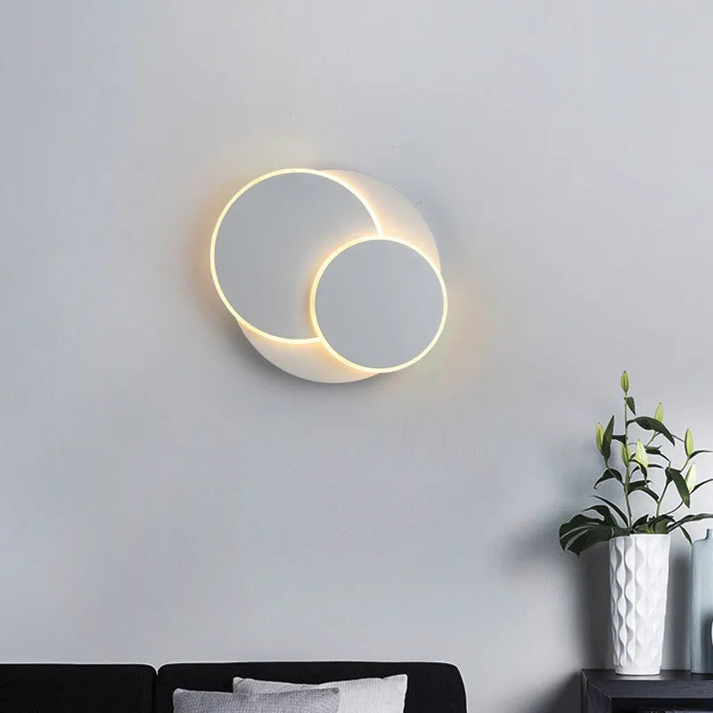 Modern round acrylic wall lamp in black or white, mounted on a wall with push-button switch.